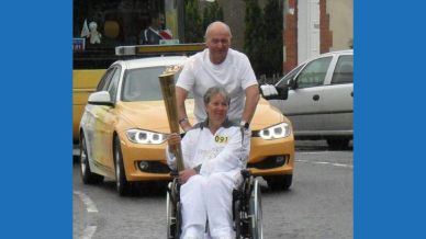 Mary holding the Olympic torch with John behind