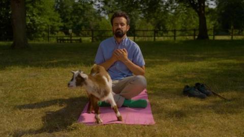 man in yoga pose with small goat