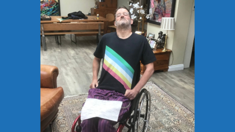 In his lounge, a 54 year-old man who thinks he looks like a teenage Arnold Schwarzenegger is sitting in his lounge in his wheelchair. He is wearing said T-shirt and some purple stuff. As well as a fabric bag holding his Suprapubic catheter. Phwooar! He has some original artwork on the wall and some nice furniture. ‘Cos he is a consumer. With dosh to spend on companies that care. He is proud and a bit tired. He needs a shave and some salad…