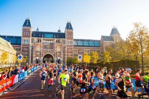 Runners taking part in the Amsterdam Marathon running around a corner in front of the iconic Rijksmuseum