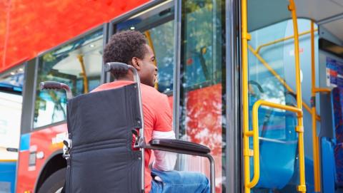 A young man in a wheelchair looks up at the doors of a bus