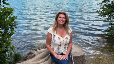 Wendi sitting by water looking at camera next to crutch