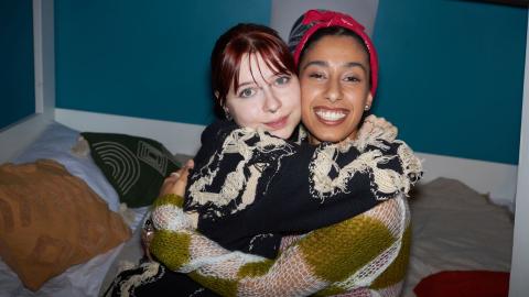 Portrait of gen Z friends sitting on bed hugging and smiling