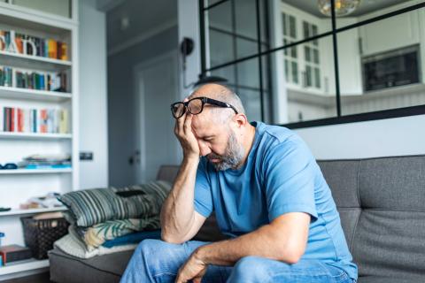 Tired man sitting on sofa rubbing eyes