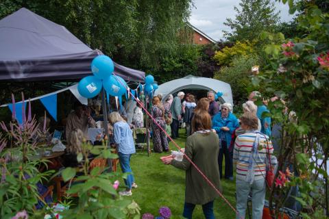 Garden party with marquees' blue bunting and balloons and groups of people standing and sitting