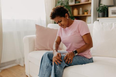 Woman on sofa holding leg in pain